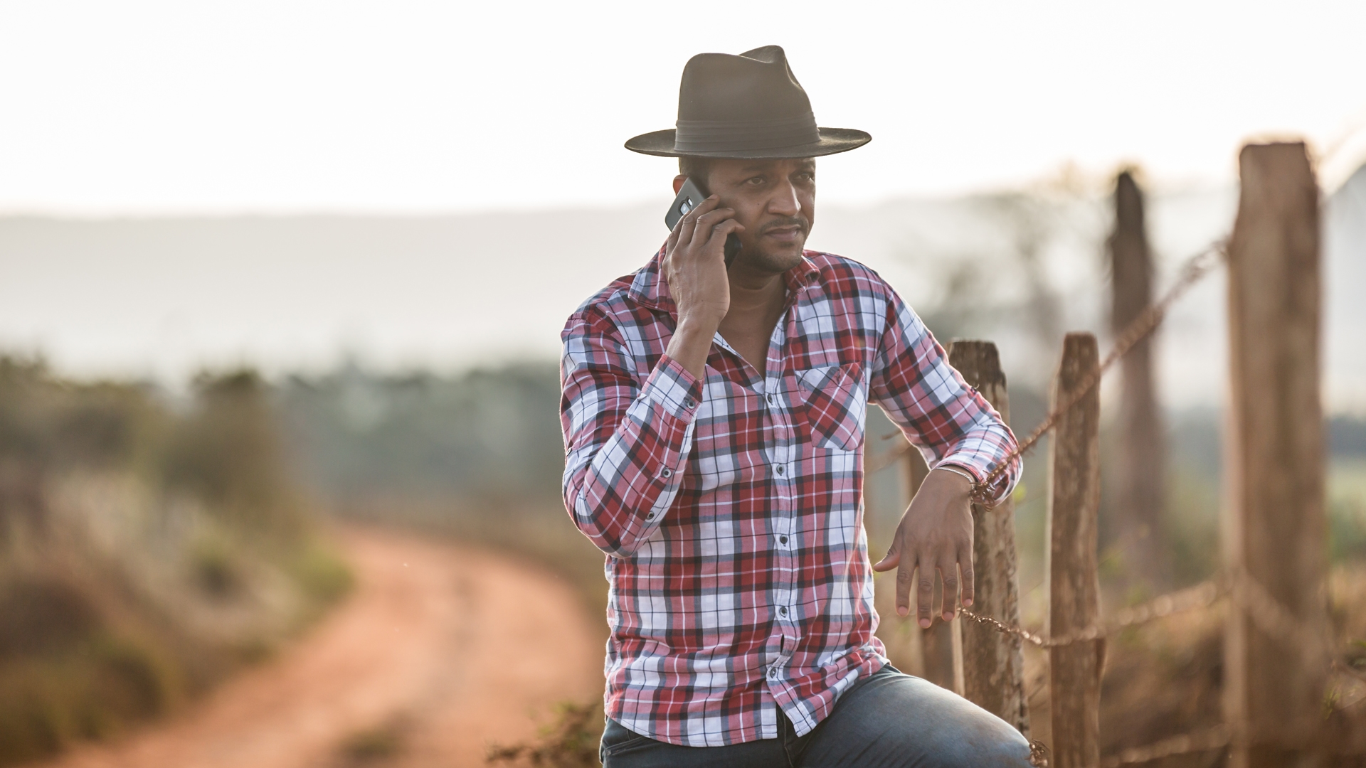 Farmer on a phone leaning against a wire fence