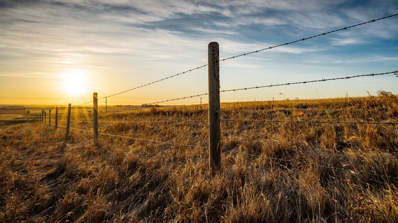 Sunrise behind a wooden barbed wire fence over natural prairie grasslands